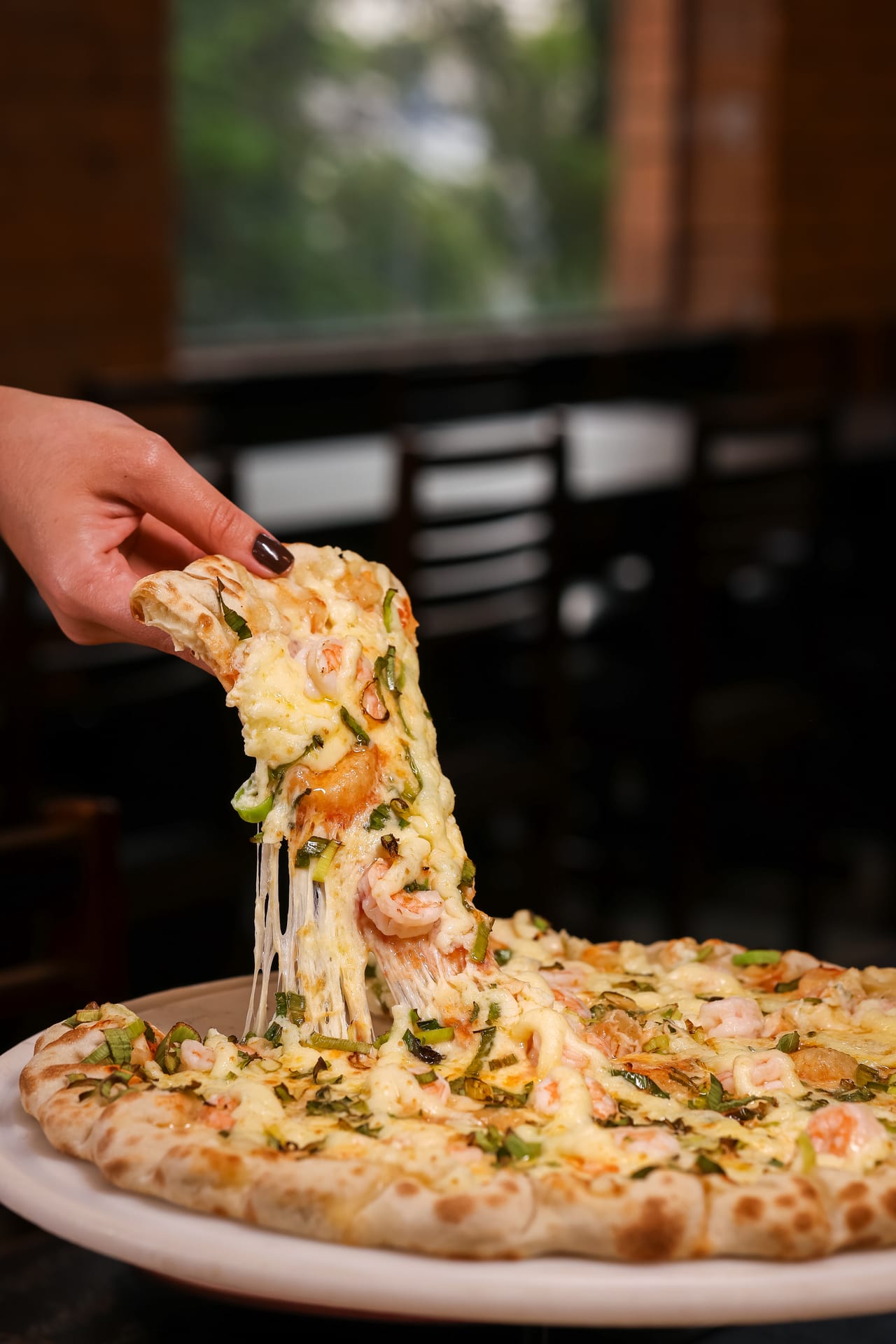 Close de fatia de pizza Øliver's com queijo puxando